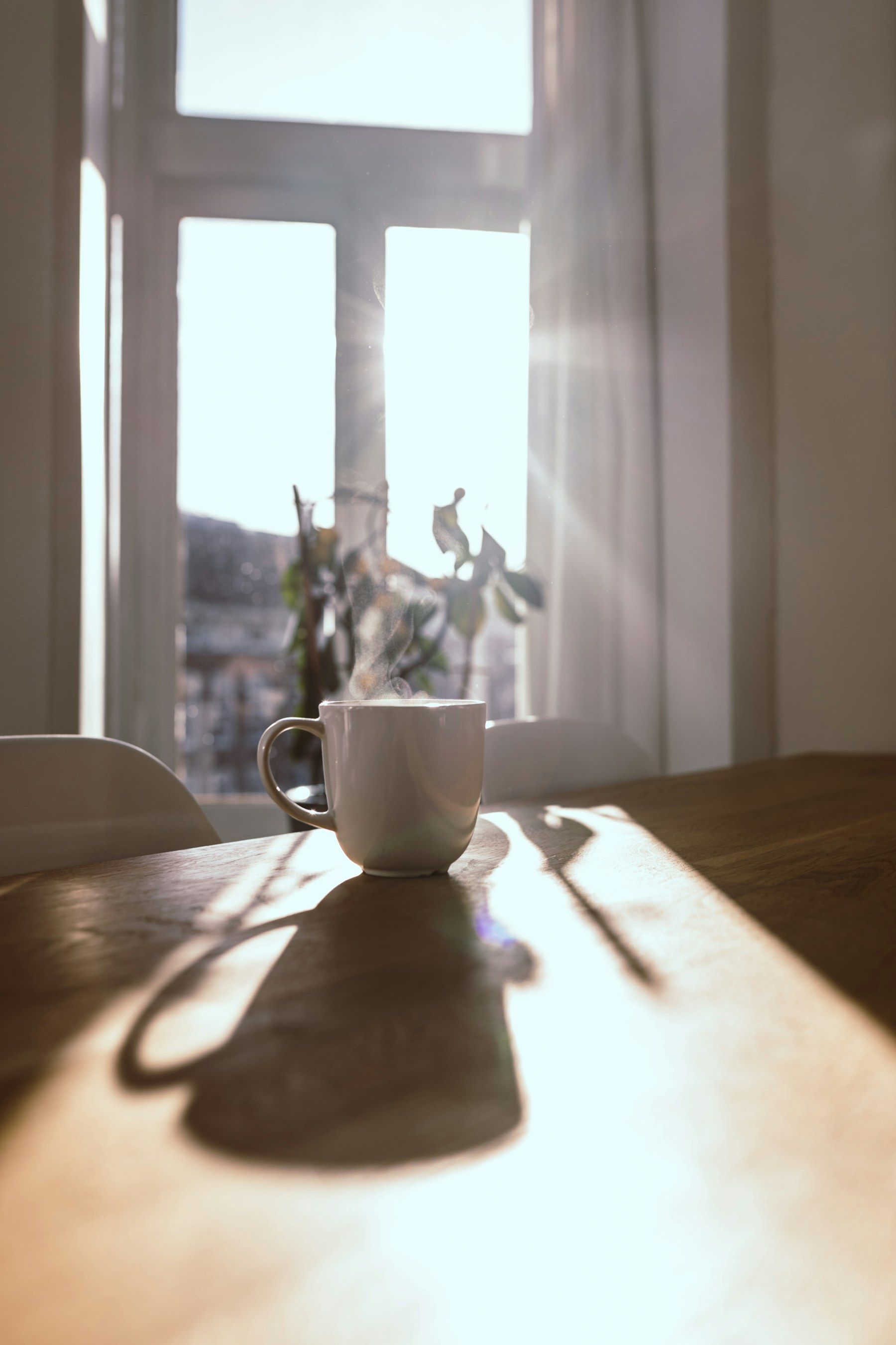 Une tasse fumante sur une table en bois, devant une fenêtre ensoleillée